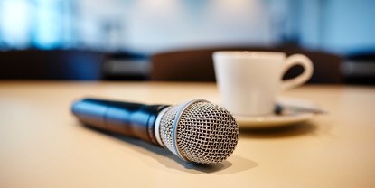 Pressekonferencestemning: mikrofon og kaffekop på et bord.